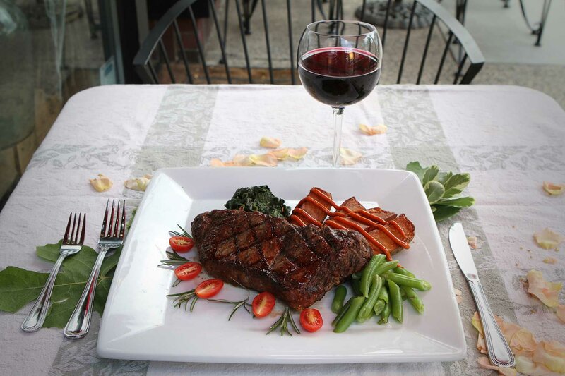 Steak entree with side of potatoes, green beans, cherry tomatoes, spinach, red tomatoes and a glass of red wine